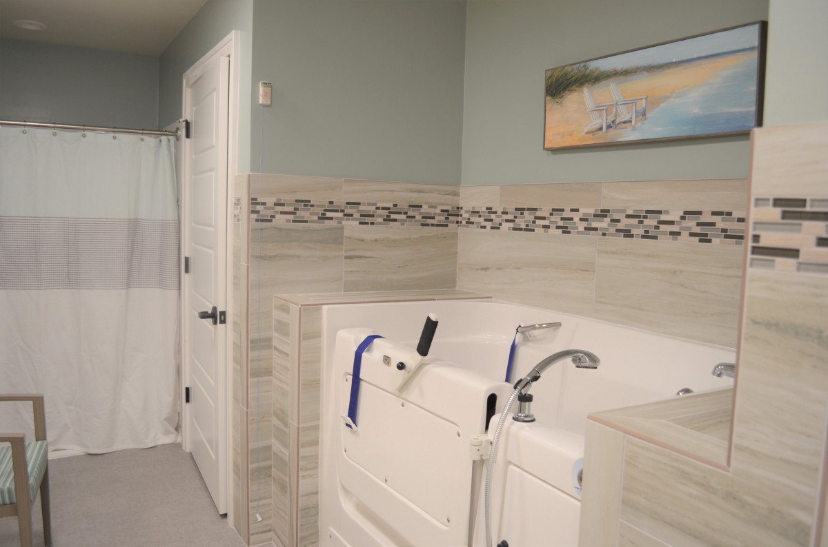 A modern bathroom featuring a walk-in tub with decorative tile accents and a serene beach painting.