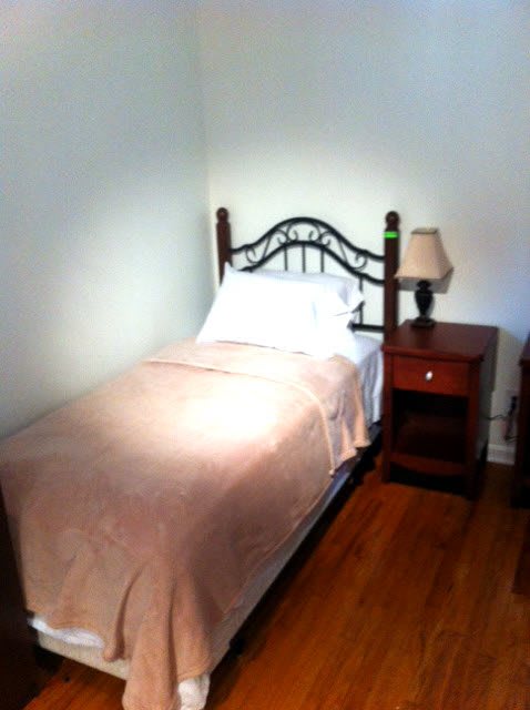 A cozy and minimalist bedroom with a single bed, nightstand, and lamp.