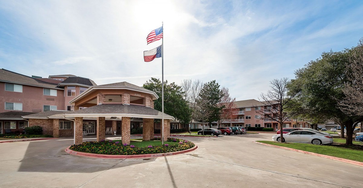 An entrance to a building complex with flags and a parking area.
