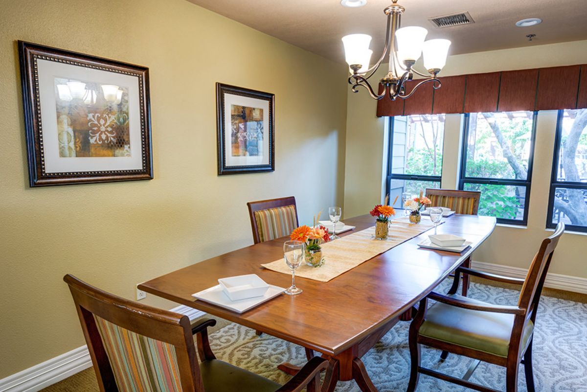 A cozy dining room with a wooden table set for a meal, adorned with flowers and illuminated by a chandelier.