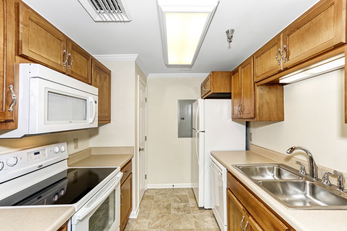 A compact kitchen with wooden cabinets, featuring a microwave, oven, refrigerator, and sink.