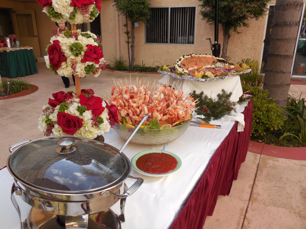 A beautifully arranged outdoor buffet with shrimp cocktail and floral decorations.
