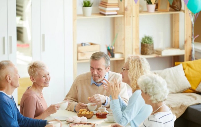 A group of seniors engaged in conversation around a table with tea.