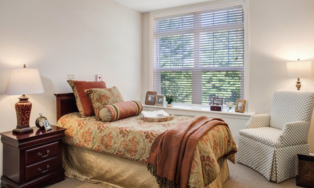 A cozy bedroom with a bed adorned with decorative pillows and a patterned blanket, featuring a large window letting in natural light.