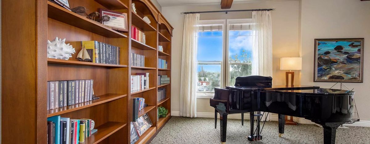 A cozy room featuring a wooden bookshelf and a piano near a large window.
