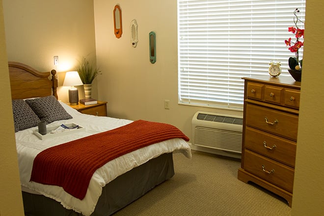 A cozy bedroom with a neatly made bed, wooden dresser, and warm lighting.