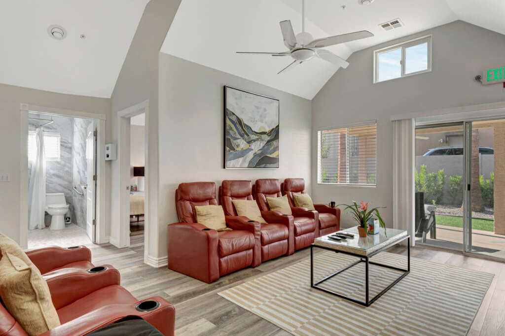 A modern living room featuring red leather sofas, a vaulted ceiling with a fan, and large windows allowing natural light to fill the space.