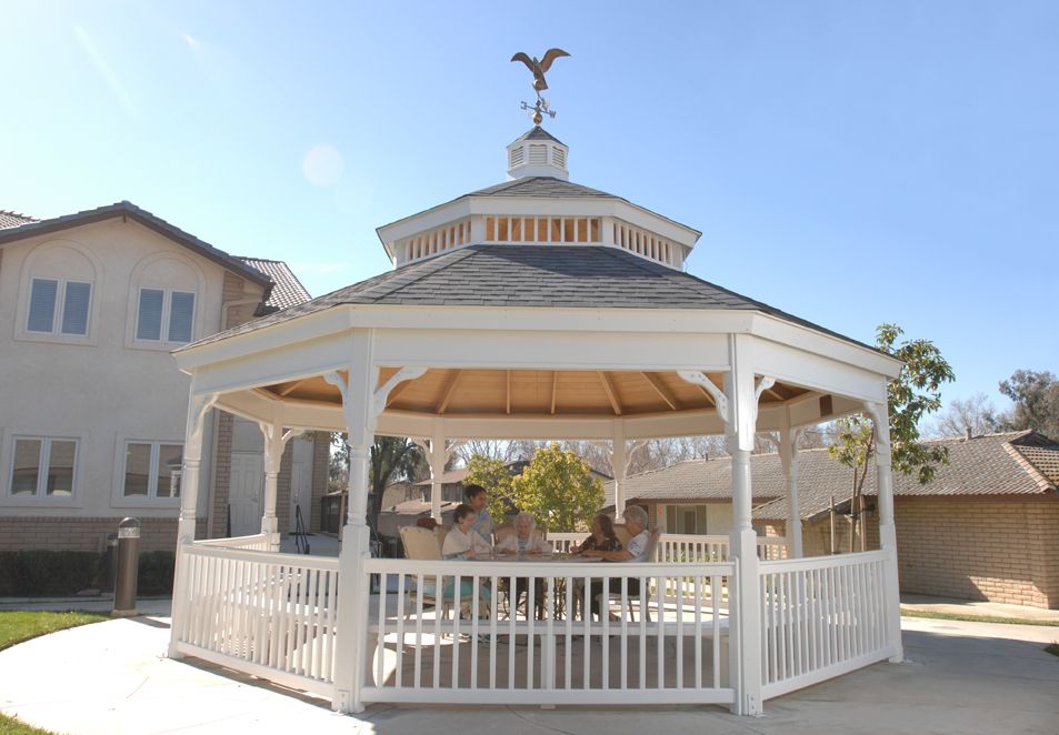 A wooden gazebo in an outdoor setting, featuring a peaked roof and open sides.