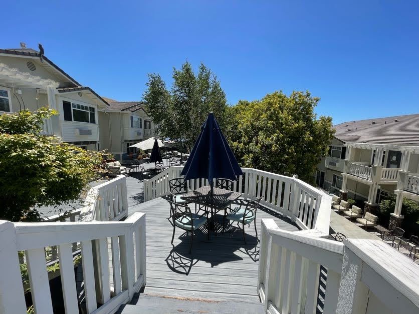 A sunny outdoor deck with patio furniture and an umbrella, surrounded by residential houses and trees.