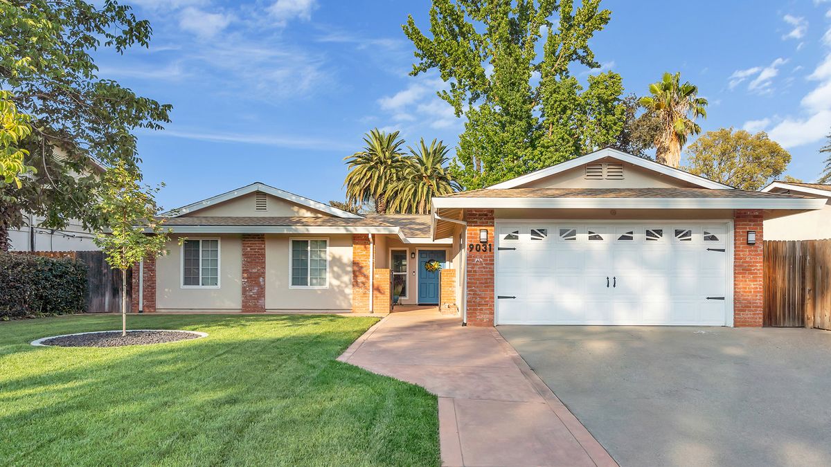 A suburban house with a well-maintained lawn, driveway, and garage under a clear blue sky.