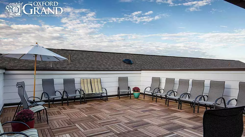 A rooftop patio with several lounge chairs, wooden flooring, and a clear blue sky.