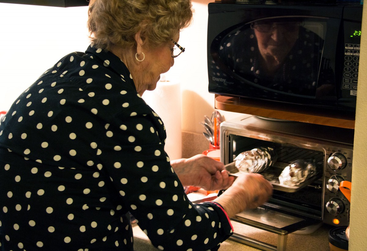 An elderly woman placing food into an oven in her kitchen.