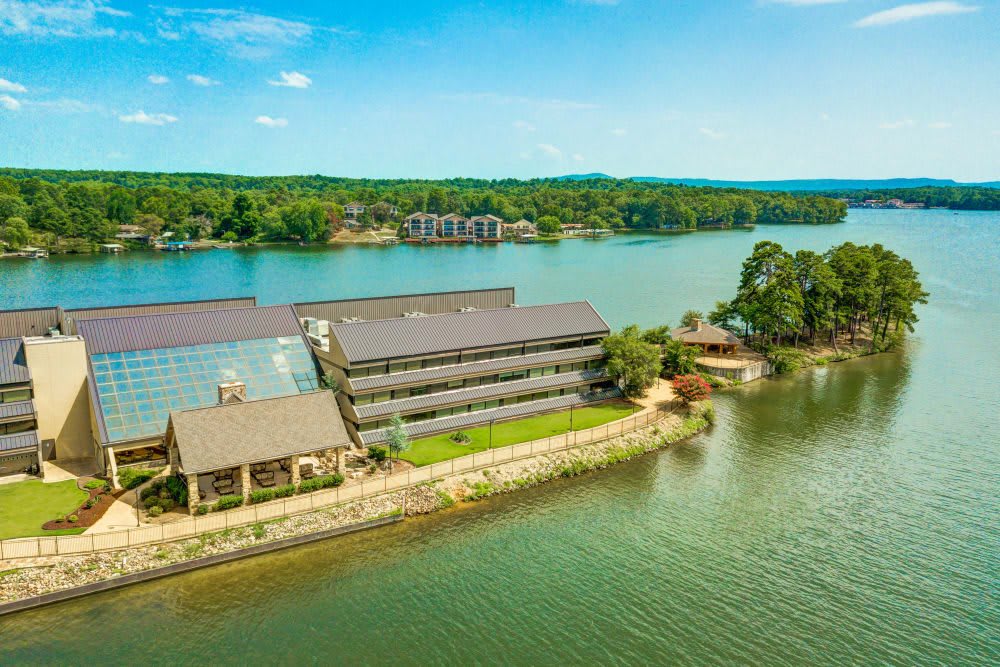 Aerial view of a waterfront building surrounded by a scenic lake and lush greenery.