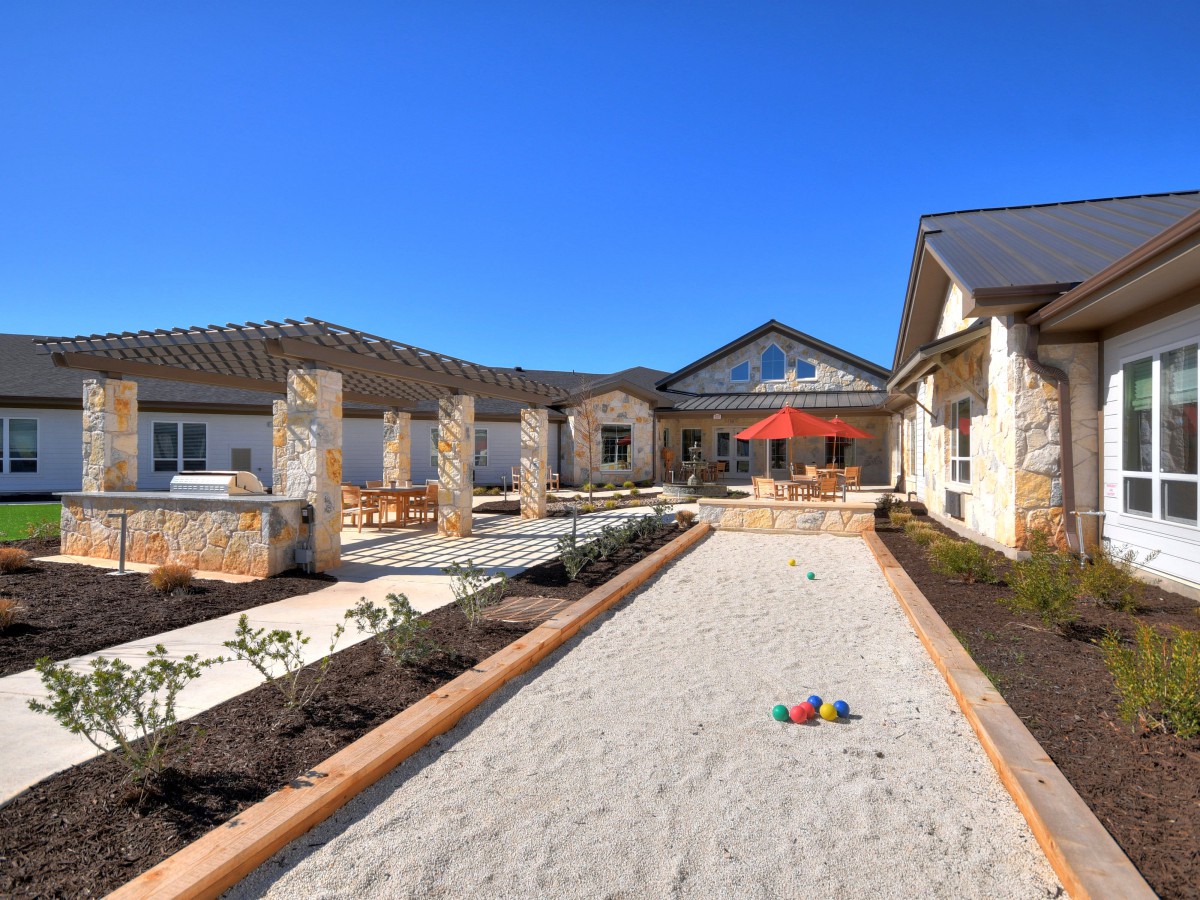 A sunny courtyard with a patio area surrounded by buildings and landscaping.