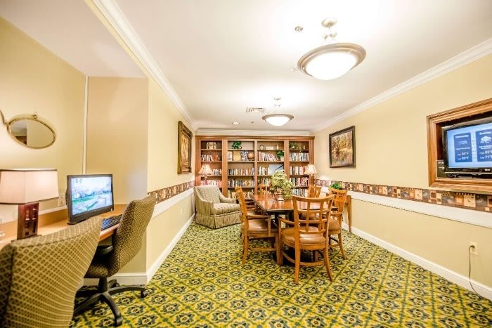 A cozy meeting room with bookshelves, a large table surrounded by chairs, and a computer desk.
