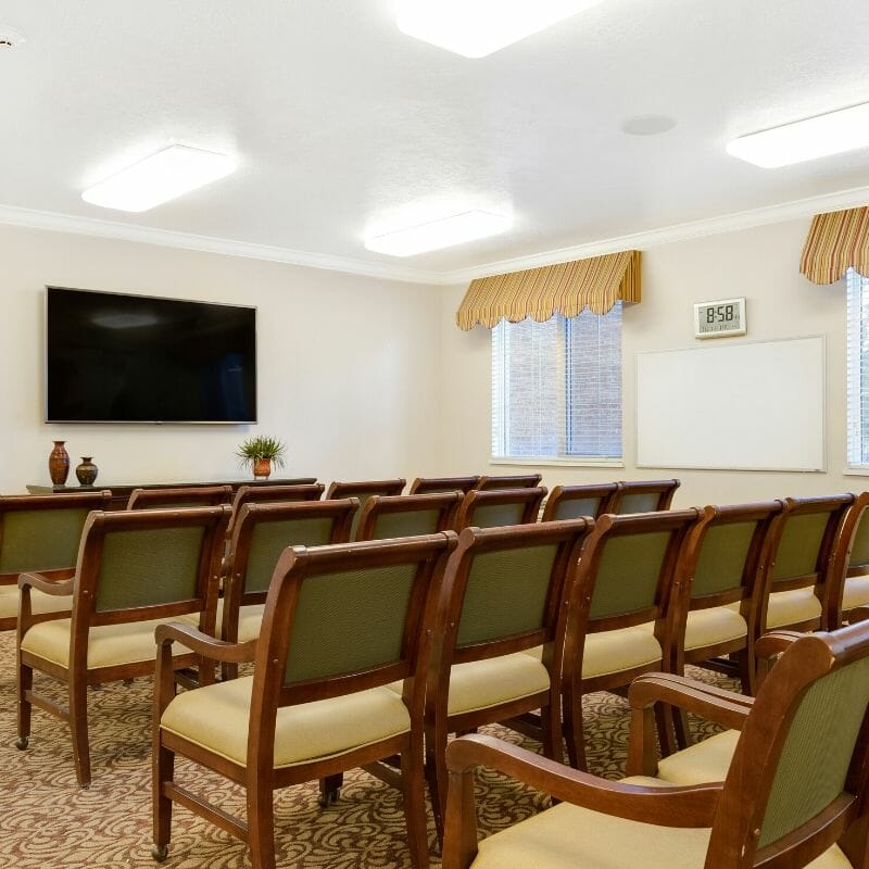 A well-lit conference room with rows of chairs facing a mounted television.