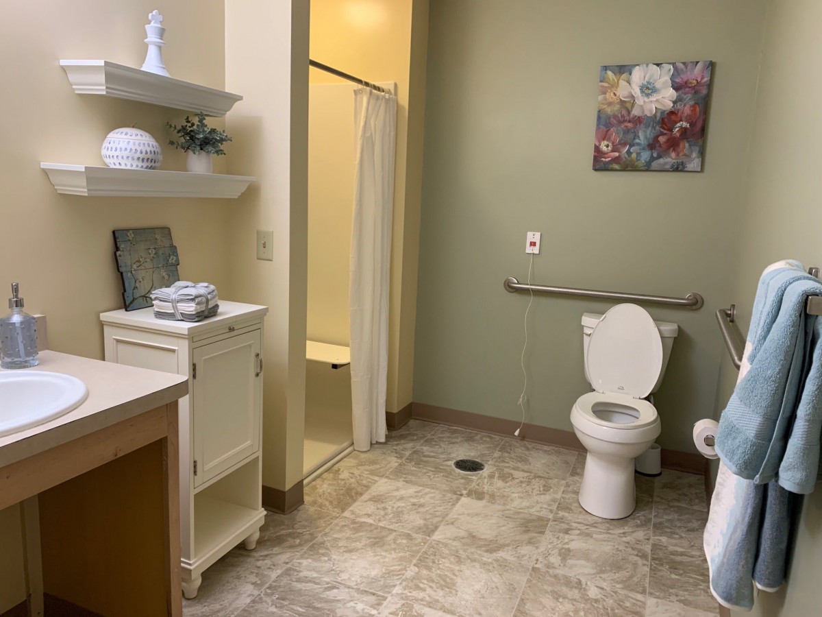 An accessible bathroom featuring a toilet, shower, and shelving with green walls.