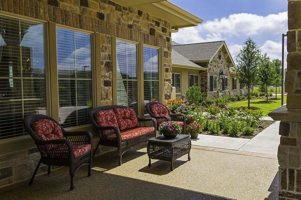 A charming patio with outdoor seating overlooks a beautifully landscaped garden on a sunny day.