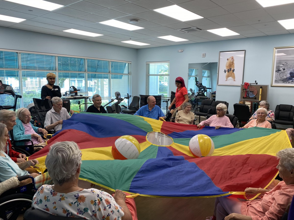 A group of seniors participates in a parachute activity at a community center.