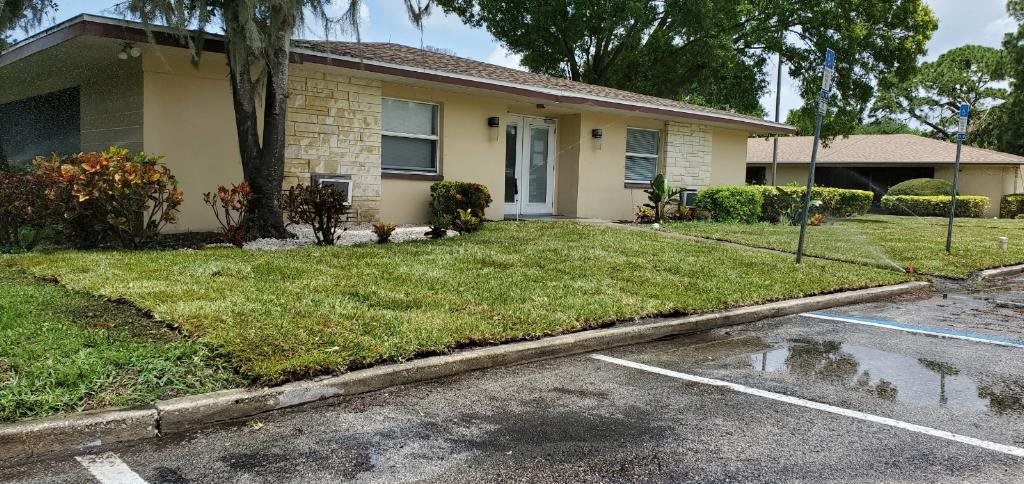 A suburban single-story house with a well-maintained lawn and adjacent parking lot.