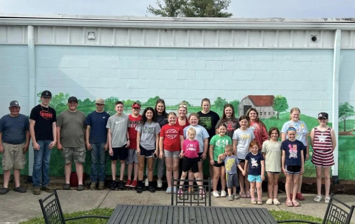 A group of people, including children and adults, standing in front of a mural outdoors.
