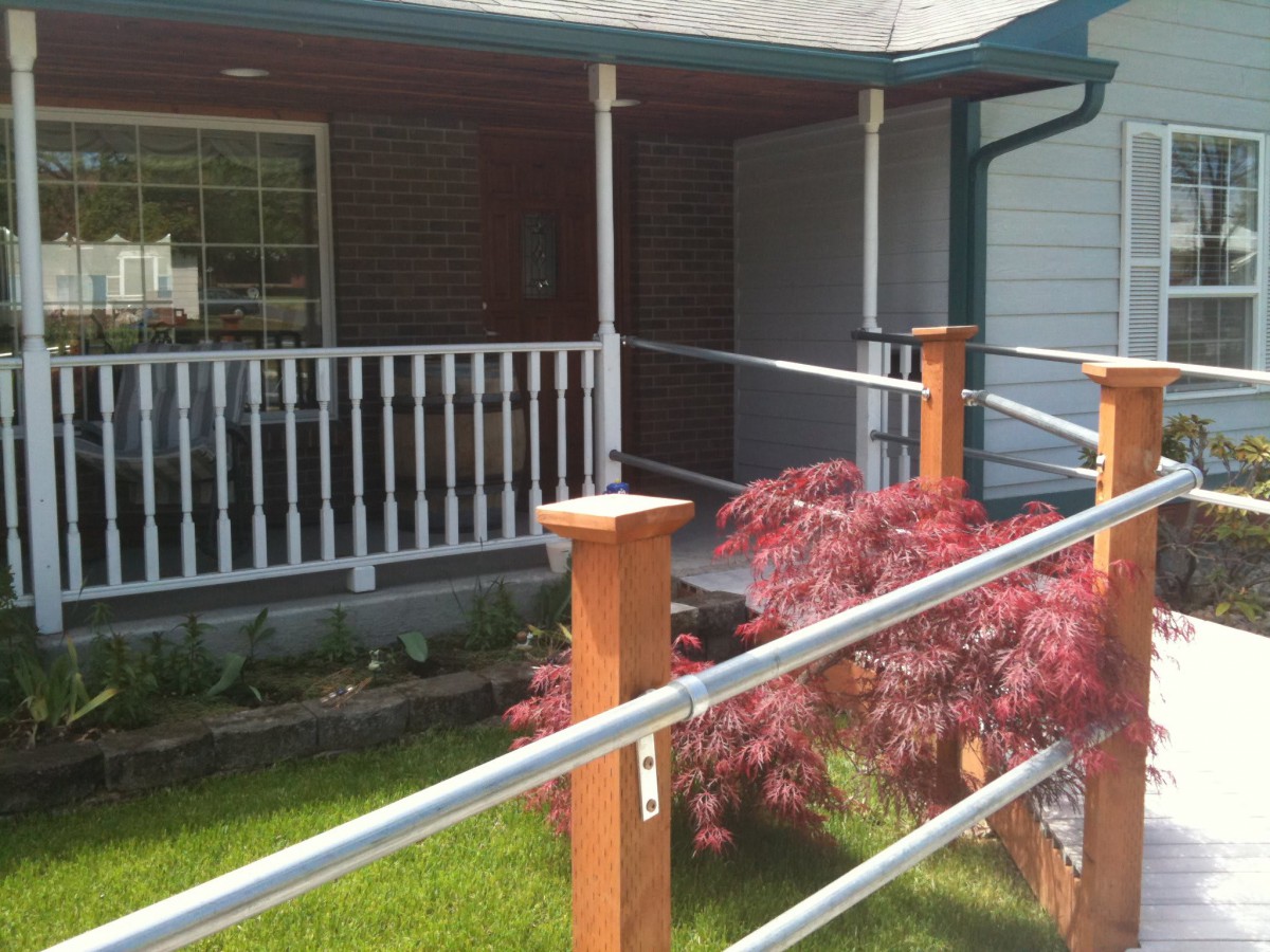 A cozy porch with a ramp and railings, surrounded by greenery and a small maple tree.