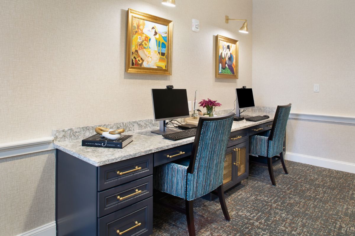 A modern office workspace with two computers, comfortable chairs, and decorative artwork on the walls.