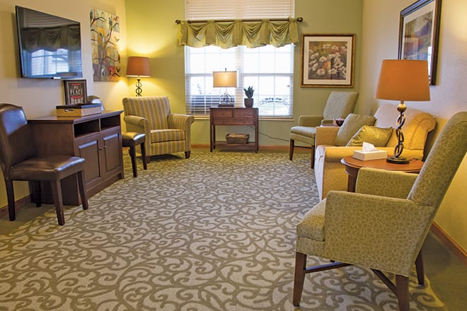A cozy living room with patterned carpet, upholstered chairs, a sofa, and several lamps.