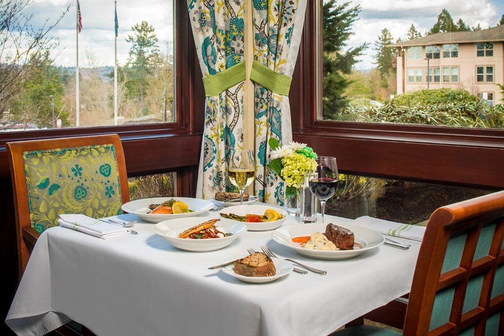 A beautifully set dining table by the window with a meal and wine glasses.