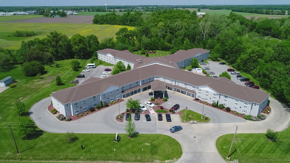 Aerial view of a large building complex surrounded by greenery and a parking area.