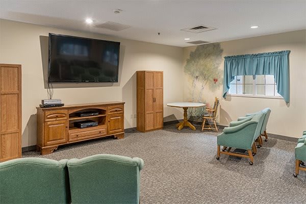 A cozy living room with a television, comfortable chairs, and a wooden cabinet.