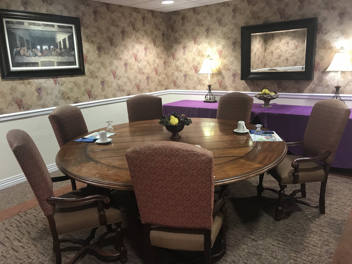 A cozy meeting room with a round wooden table surrounded by upholstered chairs, complemented by decorative wallpaper and soft lighting.
