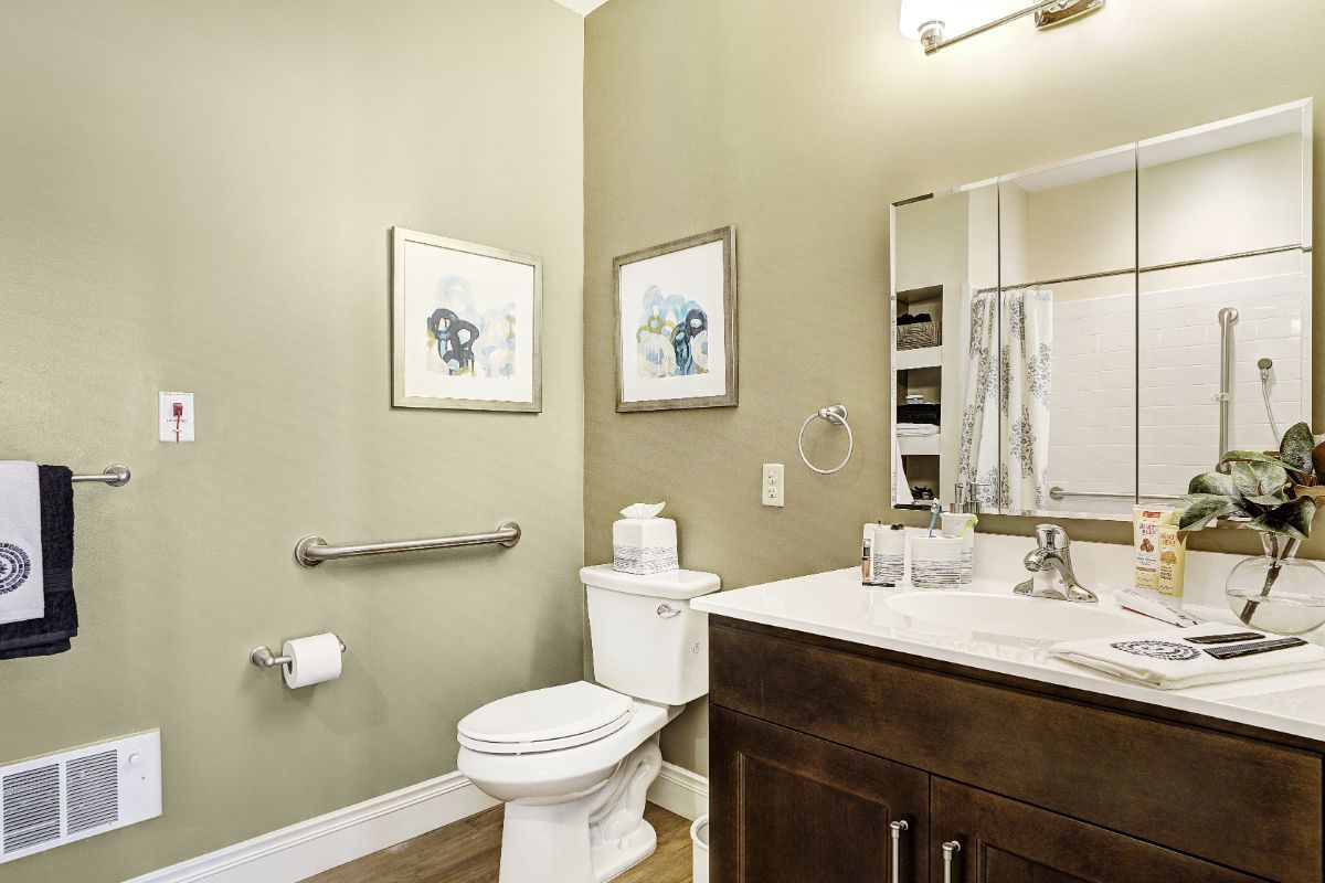 A modern bathroom with a toilet, sink, mirror, and artwork on the walls.
