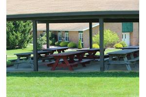 A covered picnic shelter with several tables situated in a grassy outdoor area near a building.