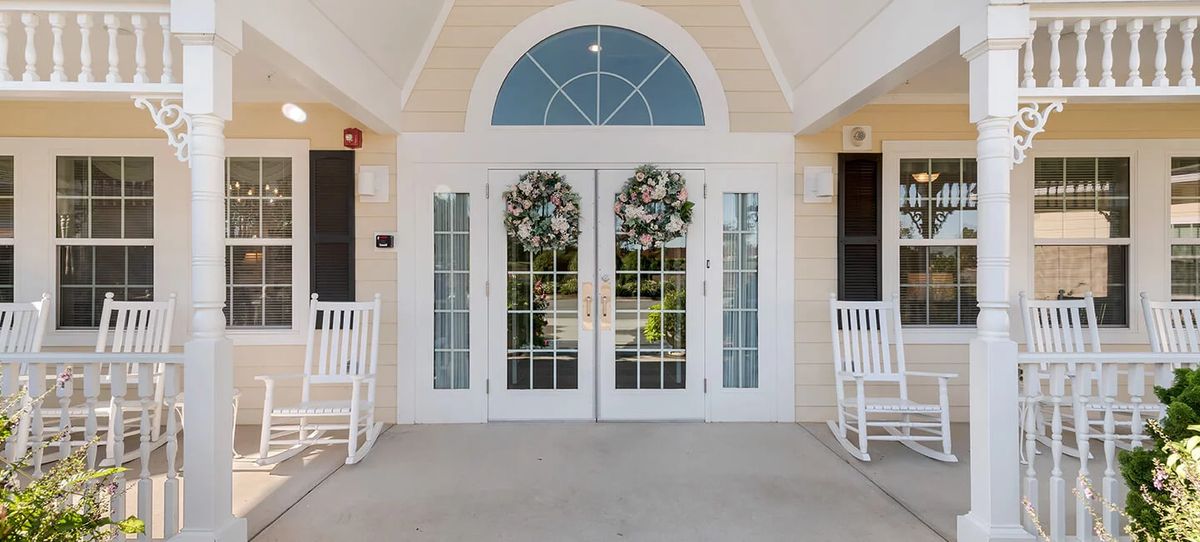 A welcoming entrance with white double doors adorned with wreaths and flanked by rocking chairs.