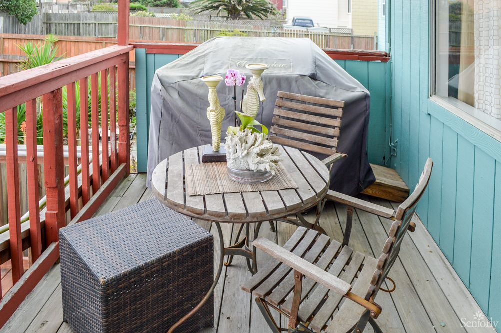 A cozy outdoor patio setup with a wooden table and chairs, a covered grill, and decorative plants.