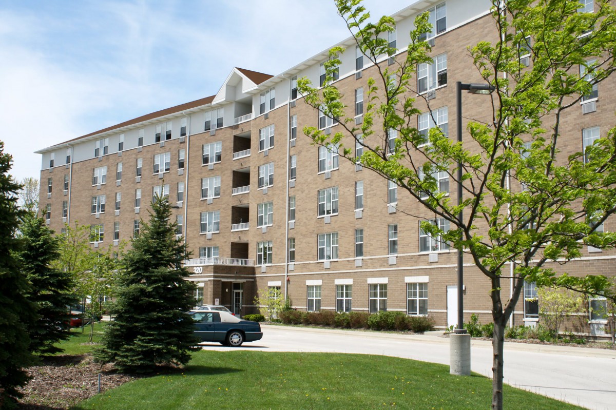 A brick residential building with a parked car and greenery on a sunny day.