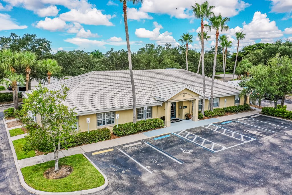 A small office building with a parking lot and palm trees under a cloudy sky.