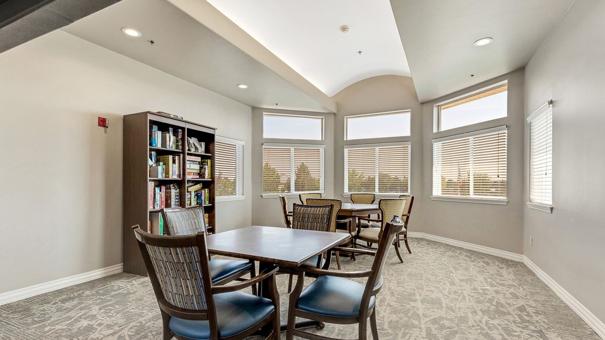 A quiet library reading room with tables, chairs, and a bookshelf.