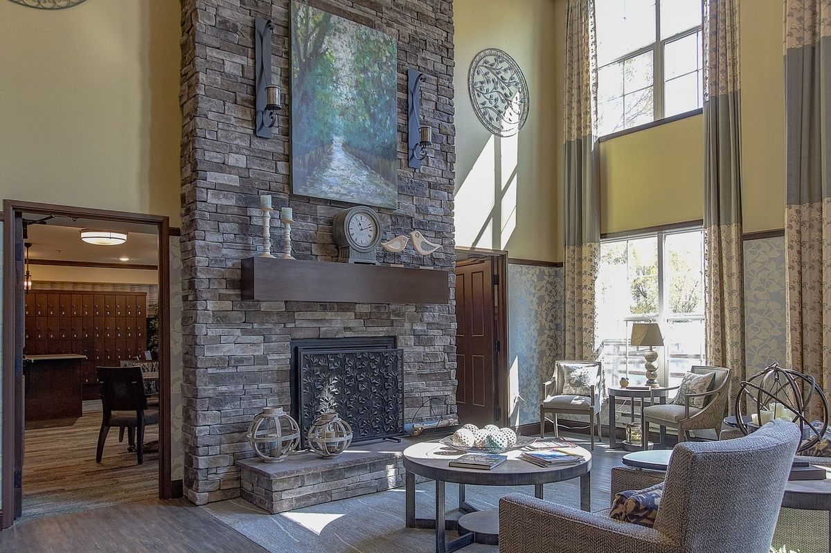 A cozy living room with a stone fireplace and high ceilings, featuring artwork and ample natural light.