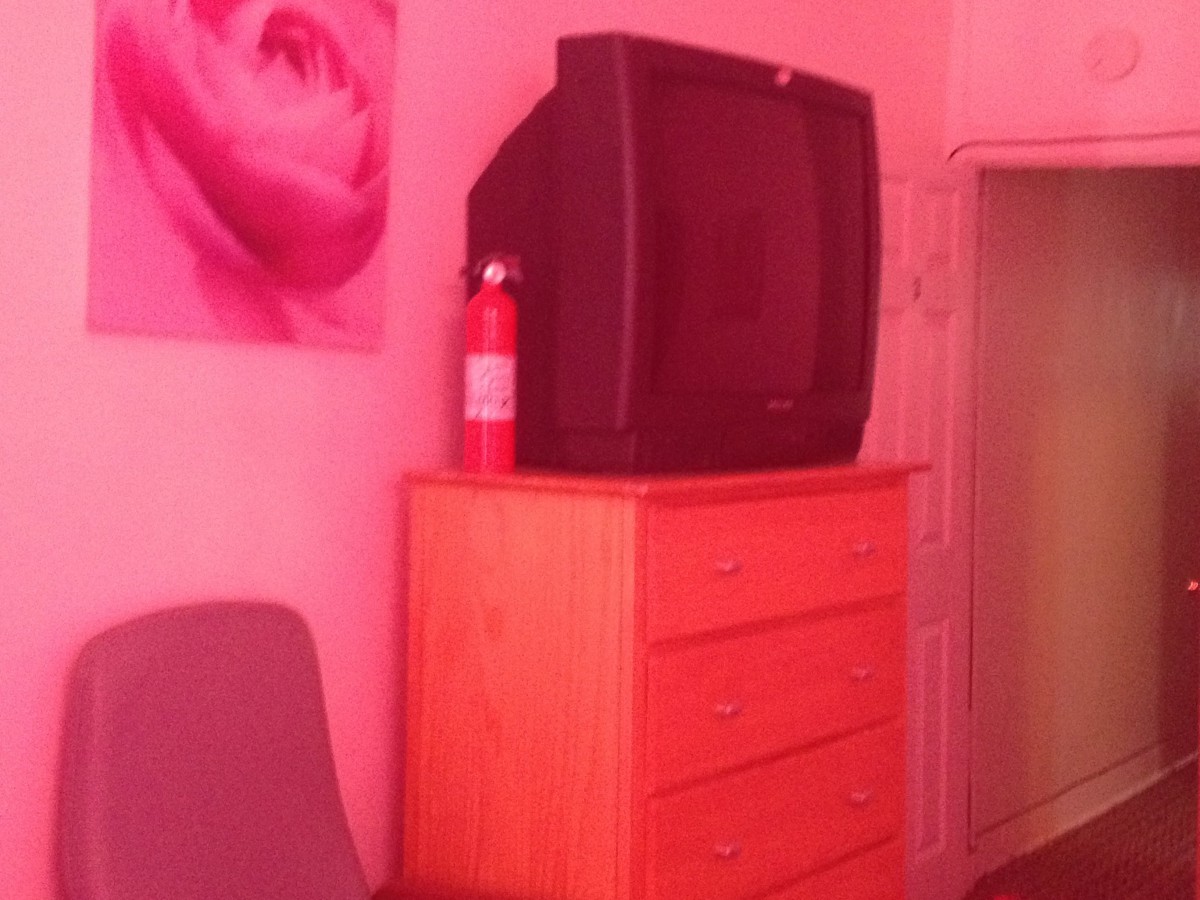 A retro television sits on a wooden dresser next to a fire extinguisher in a pink-lit room.