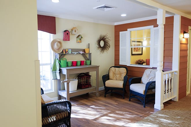 A cozy living room with armchairs and decorative shelves, featuring hats and plants.