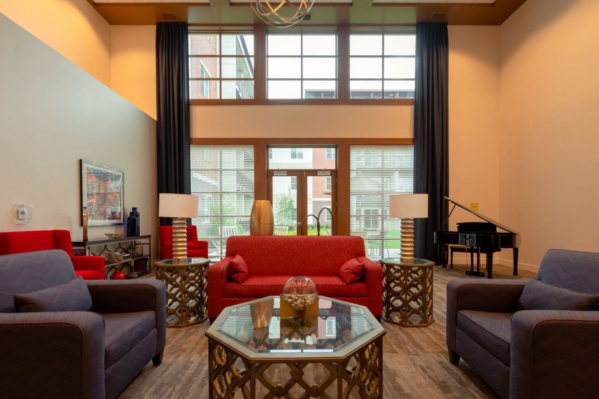 A stylish living room featuring a red sofa, modern coffee table, and a piano, with large windows allowing natural light to fill the space.