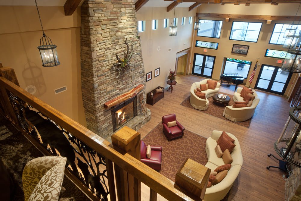 A cozy living room featuring a large stone fireplace, comfortable seating areas, and wooden beams overhead.