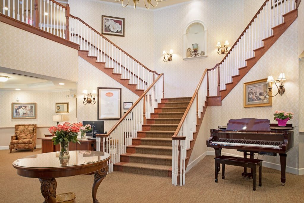 A grand interior featuring a central staircase, decorative elements, and a piano.
