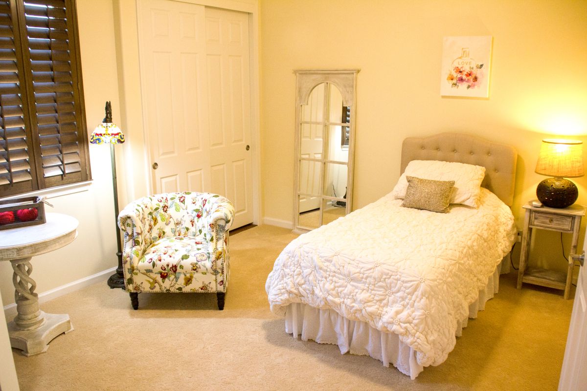 A cozy bedroom featuring a single bed with soft bedding, a floral armchair, and a tall mirror for a minimalist look.
