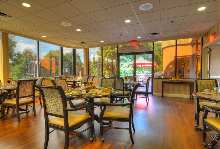 A cozy dining area with tables and chairs, surrounded by large windows letting in natural light.