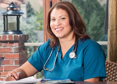 A healthcare professional in a medical uniform smiling while seated indoors.