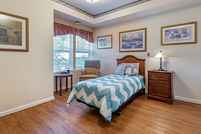 A cozy bedroom with a single bed, chair by the window, and warm lighting.