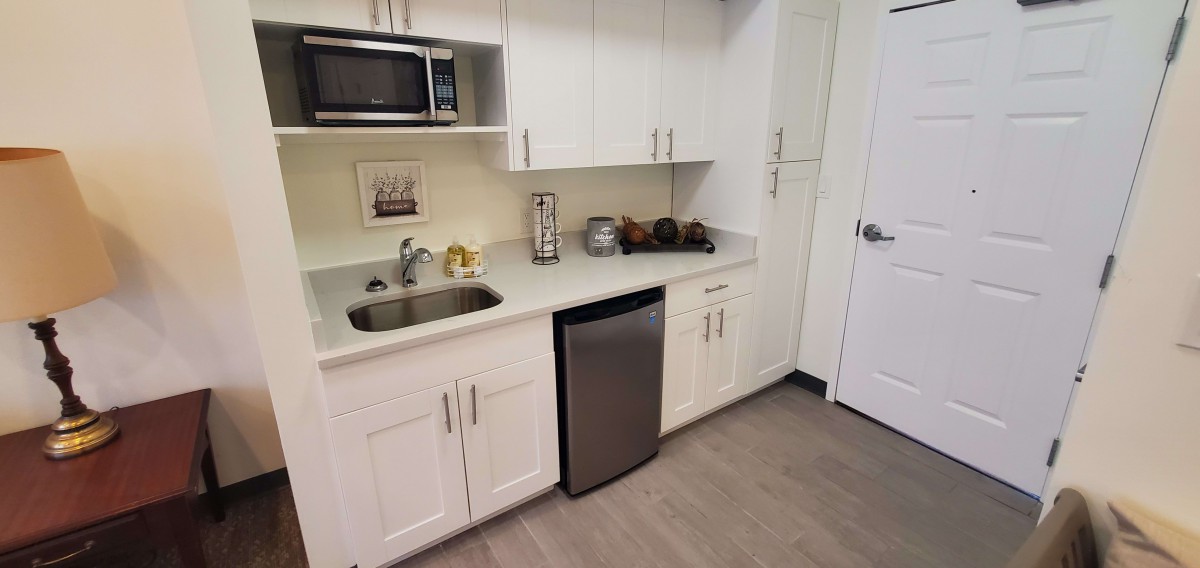 A compact kitchen area with white cabinets, a sink, a microwave, and a mini fridge.